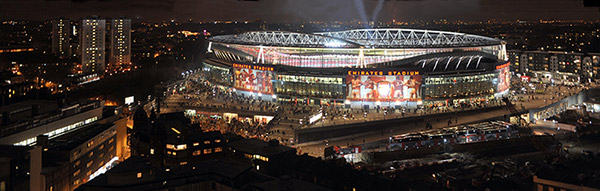 Emirates Stadium illuminated at night and showing legends on the billboard